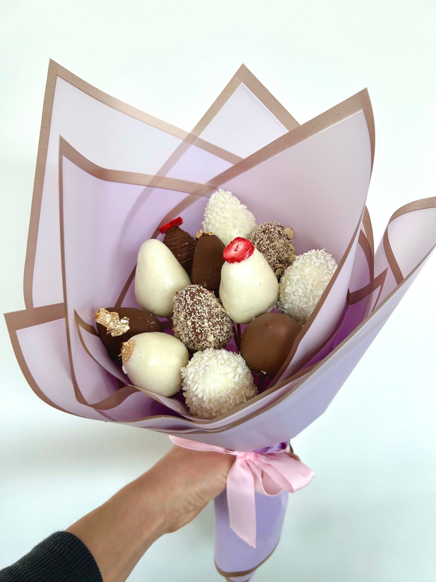 hand holds bouquet of chocolate covered strawberries in purple wrapping
