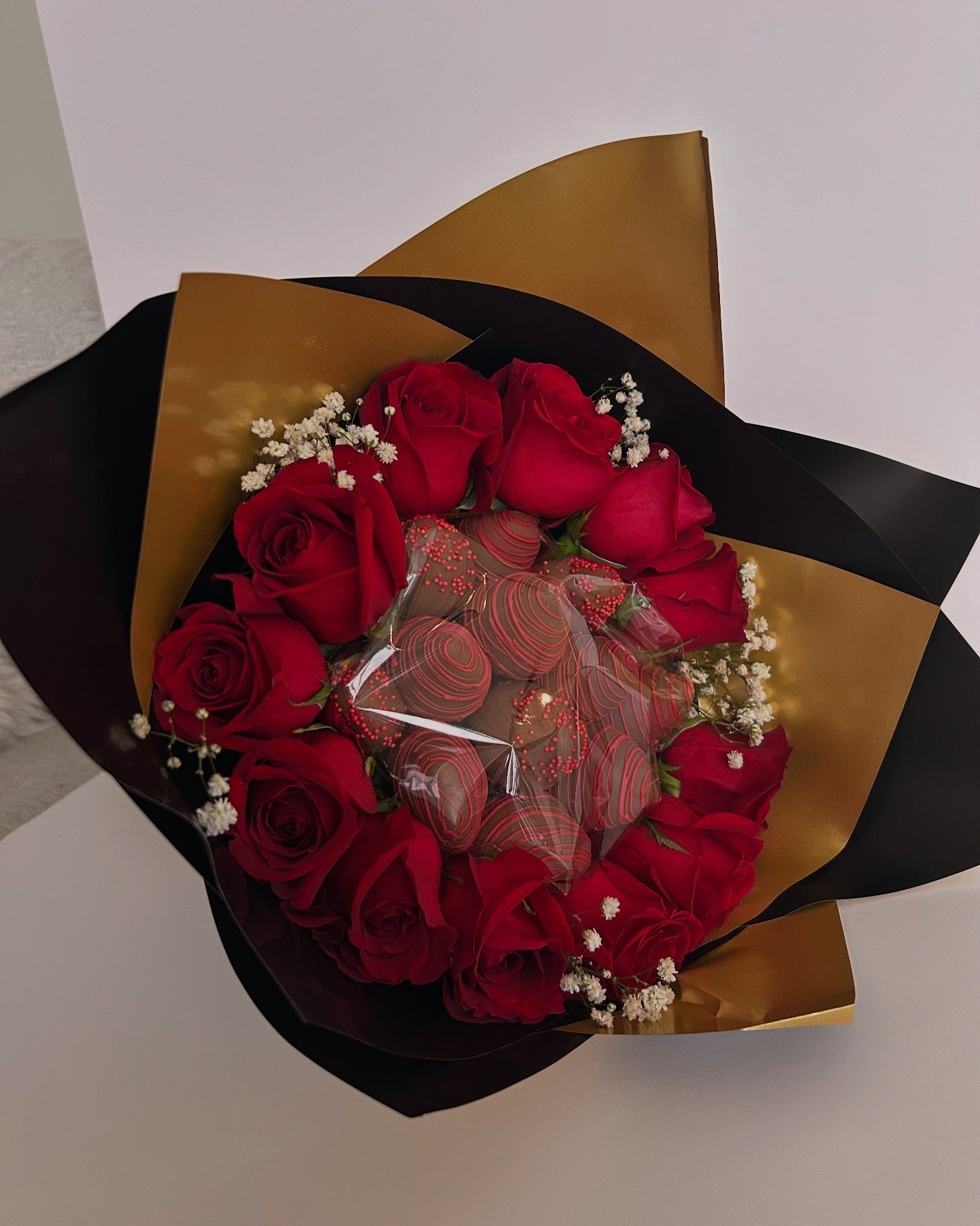 Bouquet of chocolate covered strawberries and roses with black and gold wrapping on white background
