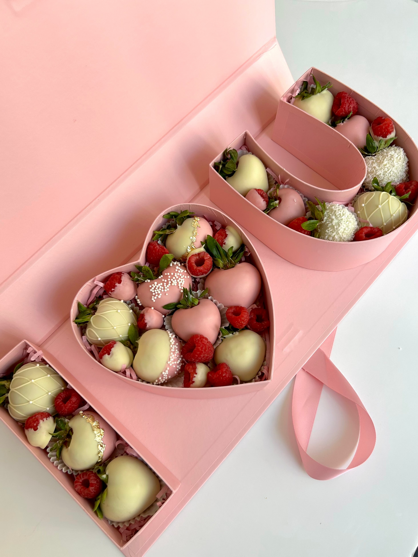 Heart-shaped pink box filled with strawberries and white chocolate candies on a white background