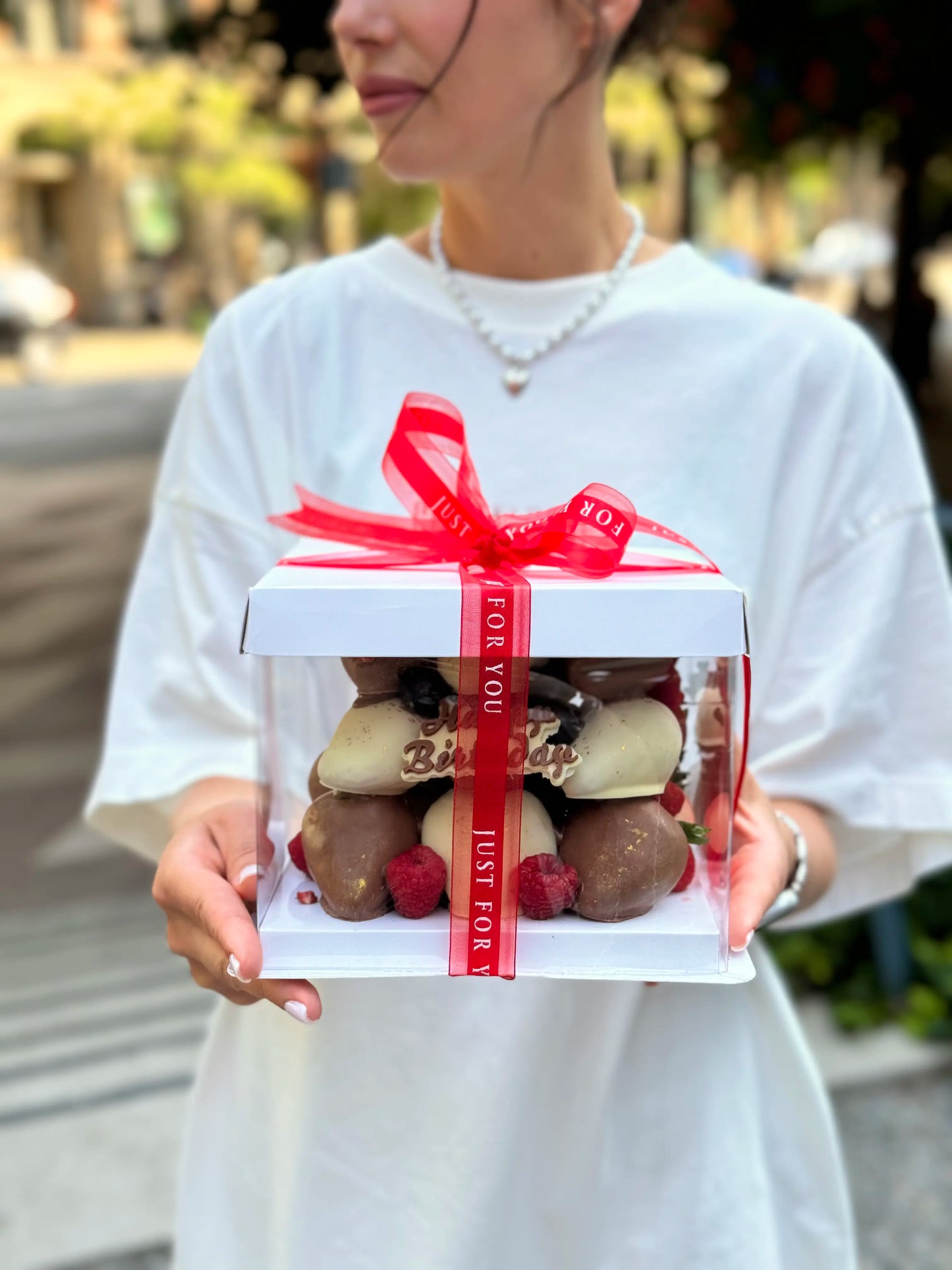 model holds chocolate dipped strawberries cake in white box with ribbon