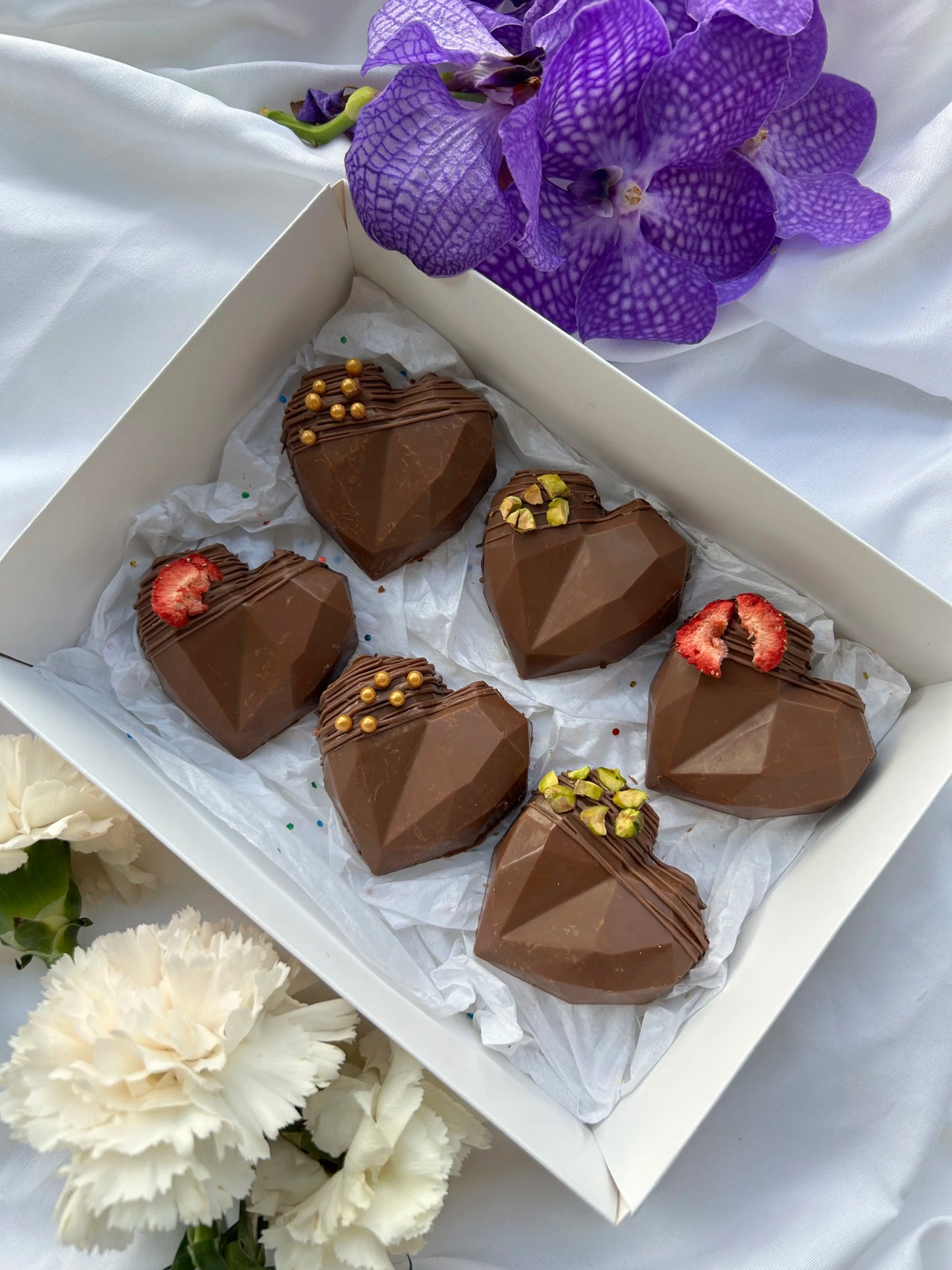 6 heart shaped dubai kunafa chocolate bars with flowers on the background