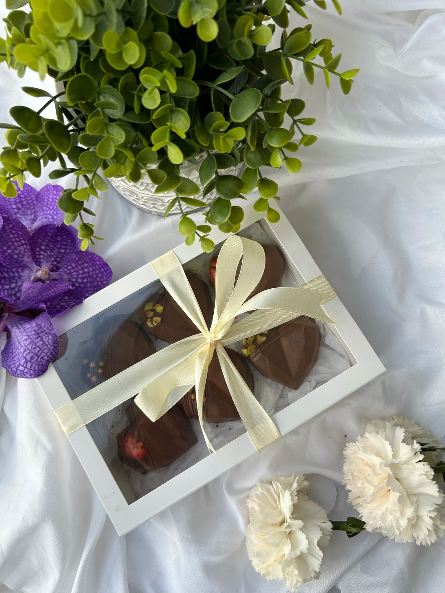 box with ribbon with dubai kunafa chocolate bars inside and flowers on the background